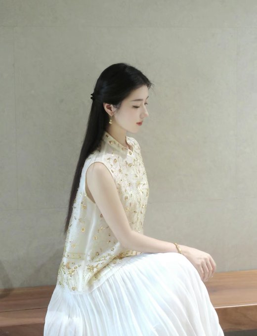 A young woman with long black hair sits in profile wearing an elegant embroidered cream vest and flowing white skirt, looking downward serenely. The image appears unrelated to the post's commentary about Bitcoin short-squeezes and market manipulation, presenting an aesthetic portrait that contrasts sharply with the financial speculation discussed.