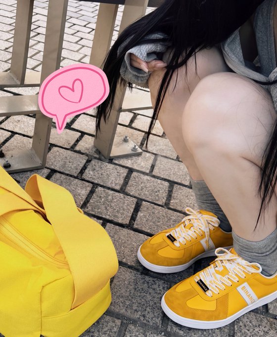 A person is crouching on a brick pavement wearing yellow sneakers with "BINANCE" printed on the side, paired with a matching yellow bag. The image showcases the Binance-branded Mid-Autumn Festival gift mentioned in the post, where the recipient thanks Binance for the cool sneakers and mentions trying out crossover steps.