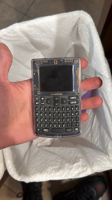 A hand holds a transparent Coldcard Mk4 Bitcoin hardware wallet, displaying its screen and QWERTY keyboard. The image accompanies the user's post about reallocating 7 figures of Bitcoin across multiple Trezor devices in different states following the recent cold storage data breach news.