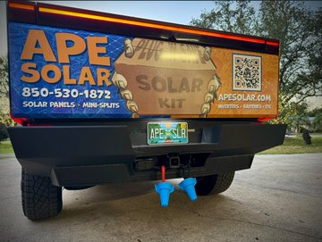 The back of an Ape Solar company vehicle displaying branding for 'APE SOLAR' with phone number '850-530-1872' and website 'apesolar.com', advertising 'SOLAR PANELS - MINI-SPLITS' and a 'SOLAR OFF GRID KIT' alongside a QR code and Florida license plate.