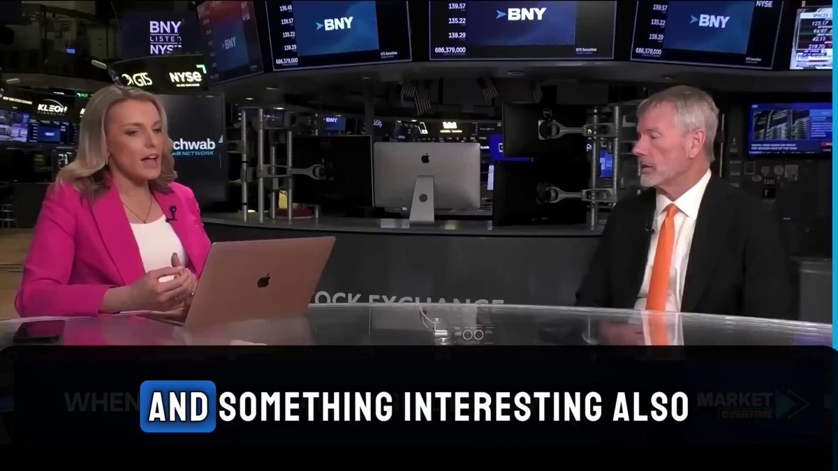 The image shows a man and a woman sitting at a desk, with a laptop open before them. A news headline for the day says "And something interesting also", which implies that there might be an interesting or unusual aspect of their conversation or situation related to the photo's content. In this case, it is likely they are discussing the mining industry, specifically Bitcoins, and the massive value associated with mining operations. The image suggests the interview may have a financial context or focus on cryptocurrency trends in the market.