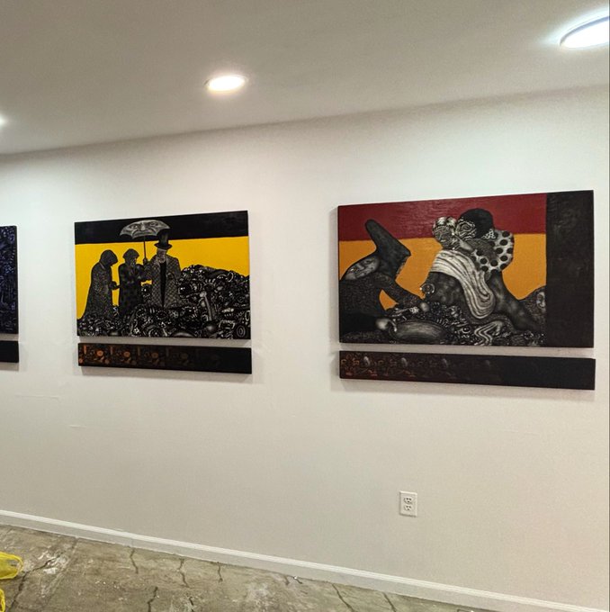Two framed artworks with black, yellow, and red coloring hang on a white wall, featuring intricate figures and scenes.