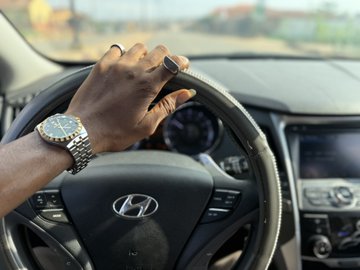 A close-up shot shows a hand gripping the steering wheel of a Hyundai, adorned with a gold and silver wristwatch, suggesting a drive that complements the post's vibe of a hustling day—turning a small $1 into $100 with @degencom and looking ahead to a better week.