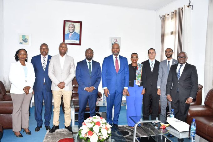 A formal group photo of nine people in business attire posing together in what appears to be an official office setting.