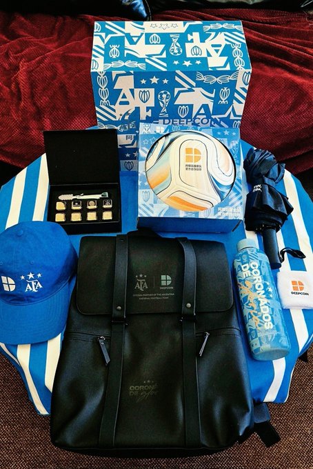 A collection of Argentina soccer merchandise is displayed, including a black "AFA" branded backpack, blue "ARGENTINA" cap, a soccer ball in packaging, "AQUA" gift box, a folded umbrella, a "Brothers" water bottle, and a black case holding small accessories, all arranged on an Argentina-themed cloth.

The image showcases Argentina fan gear and prizes, likely related to a World Cup giveaway or match-day promotion, tying into the post's discussion about betting on an Argentina vs. Egypt soccer match.