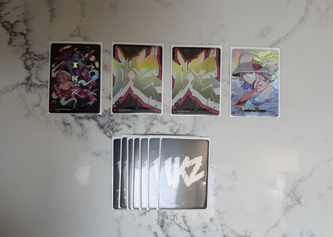 Five collectible trading cards arranged on a marble surface - four showing anime-style artwork (three with lightning bolt designs, one with a character in a hat) and five cards face-down with a 'WKZ' logo.