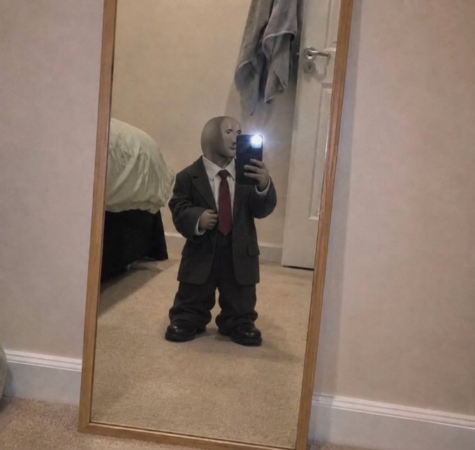 A small figure in a formal suit, red tie, and featureless mask takes a mirror selfie with a phone, the flash illuminating the reflection. The accompanying caption humorously pairs with the image, suggesting the suited "stonk market" trader is always on the clock—dressed for business even at home.