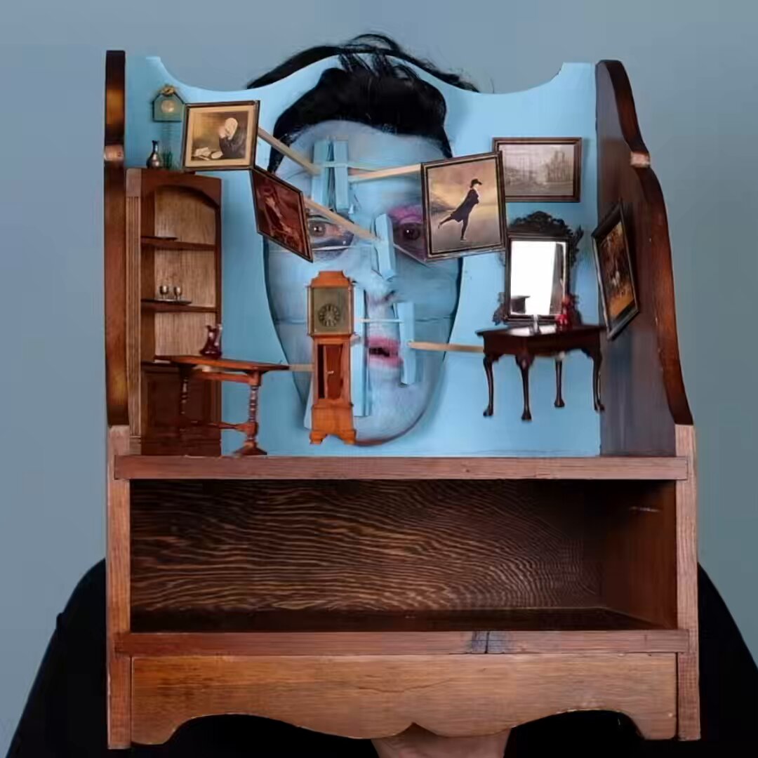 The image features a wooden shelf with various items, including a face made out of wood that appears to be a person's head. The shelf also has pictures hanging from it, giving the impression of a miniature room or display. A person can be seen in the background, possibly admiring the unique and creative arrangement of the objects on the shelf.