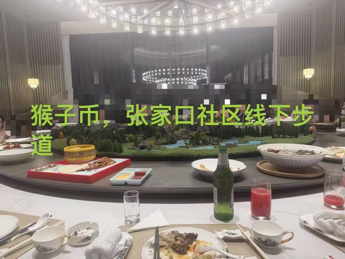 A formal dining table set with various dishes, a green bottle, and drinks, with Chinese text overlay reading '猴子币，张家口社区线下步道' (Monkey Coin, Zhangjiakou Community Offline Trail).