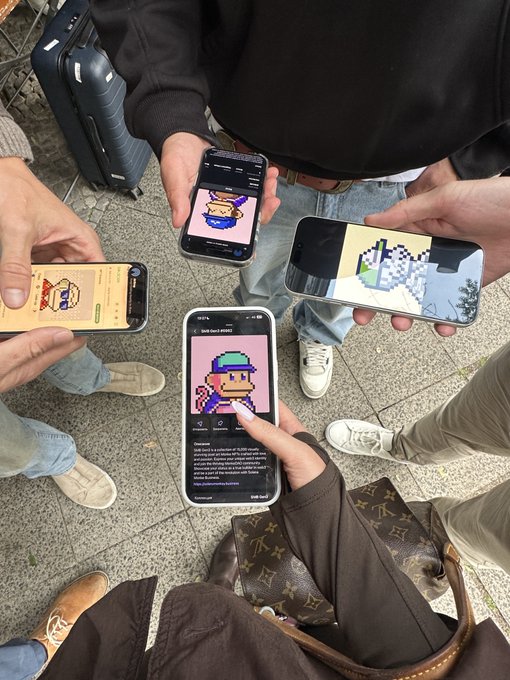 Several people hold smartphones showing pixel-art NFT-style characters and a 3D scene while standing outdoors.