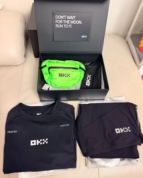 Merchandise items including a black long-sleeve shirt, black shorts, and a green waist bag, all branded with 'OXX', displayed near a box reading 'DON'T WAIT FOR THE MOON FUN TO IT'.