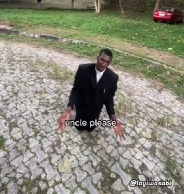 A man in a black suit kneels on a stone pavement with his arms outstretched, with the caption "uncle please" and the handle "@layiwasabi" visible.