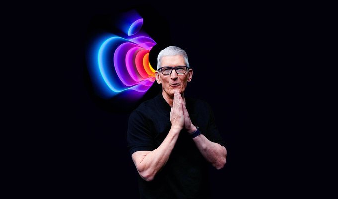 Tim Cook stands with his hands pressed together in a greeting gesture, positioned in front of a neon rainbow Apple logo on a dark background.
