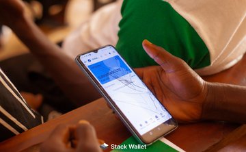 A close-up photograph of a person holding a smartphone displaying a digital payment or navigation app with 'Stack Wallet' visible at the bottom.