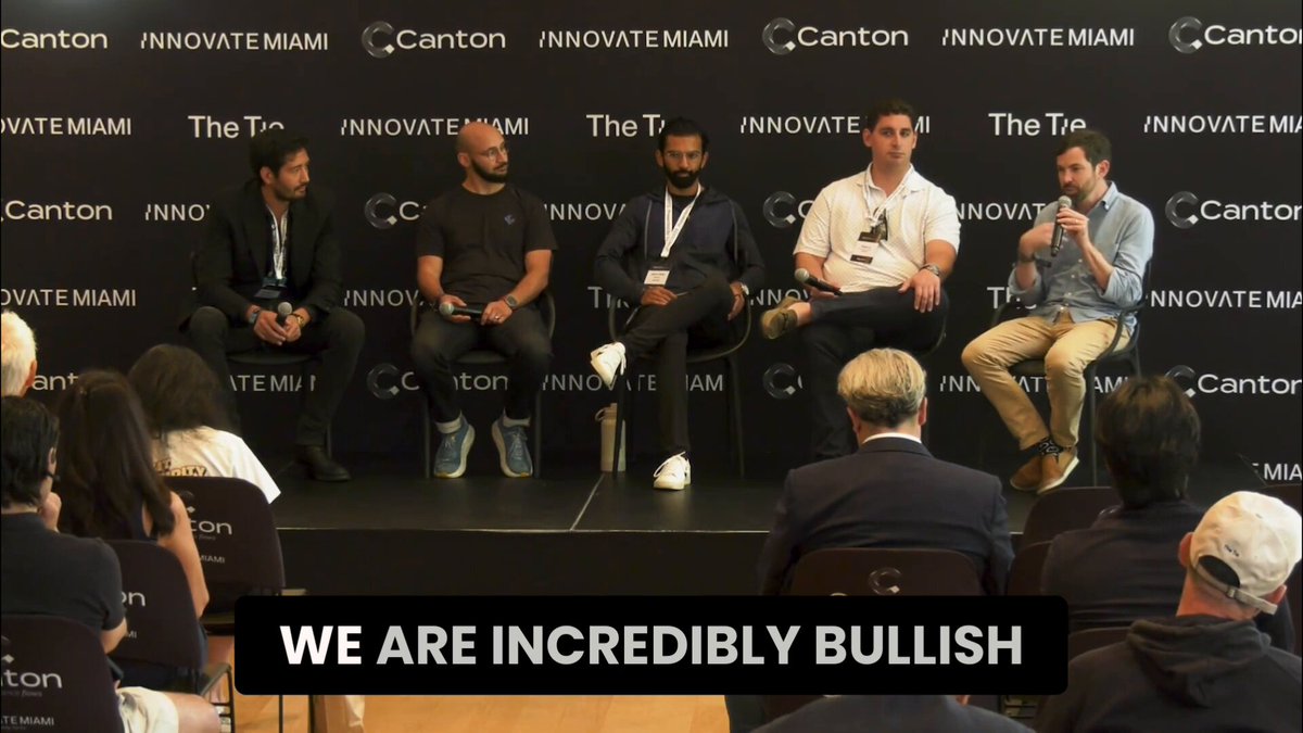 The image shows a group of people sitting around a table, with some men wearing suits and others in casual clothing. They are gathered for an event or panel discussion at Innovate Miami. The backdrop features a black wall with white text that reads "We Are Incredibly Bullish". This suggests the panelists might be discussing the potential benefits and opportunities presented by crypto tokens, particularly those without any investors' protection.