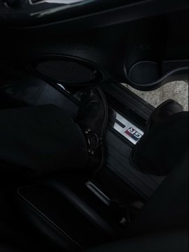 A view inside a dark car showing a person's legs and shoes near a door sill with an "RS" badge.