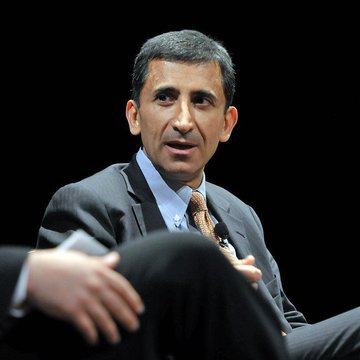 Faryar Shirzad, Coinbase's chief policy officer, is shown seated and speaking, likely at a public forum or panel discussion, as he advocates for the CLARITY Act and criticizes banks that simultaneously embrace crypto while lobbying against clear regulatory frameworks.
