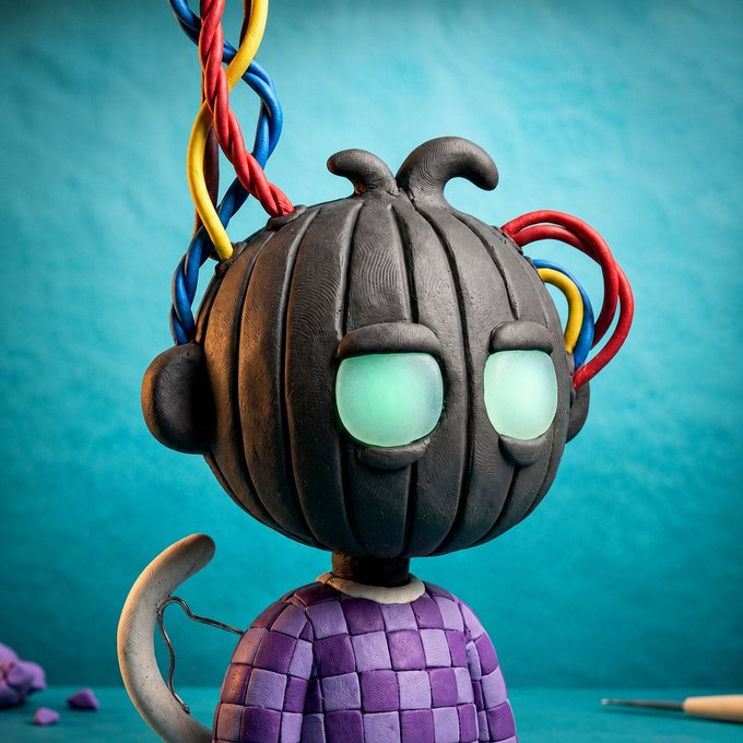 A 3D-rendered character with a pumpkin-like head, glowing green eyes, and colorful wires emerging from the top, wearing a purple checkered shirt against a teal background.