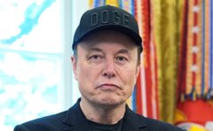 The image features a man wearing a black baseball cap with the word "DOGE" written on it, sitting against a blue background. There are also several colorful flags behind him, adding visual interest to the scene. The caption below the image reads "Bitcoin is Energy Money". This suggests that Bitcoin has been linked to energy consumption and its use as an alternative or supplement to traditional currency systems.