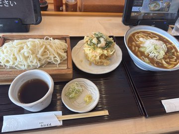 A Japanese meal set on a wooden tray featuring cold udon noodles, a bowl of curry udon, tempura with dipping sauce, and ginger garnish.