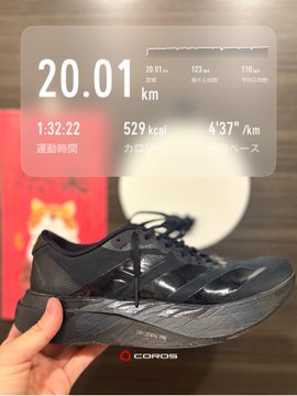 The image features a person holding up their black running shoe, which has a red sole with white text that says "トレミ" on it. The shoe appears to be worn out or used for exercise purposes. In the background of the photo, there is a small red circle with Chinese characters and numbers displayed in an app-like format. This could possibly be a fitness tracking device or a running app that provides information about distance, pace, and calories burned during a run.