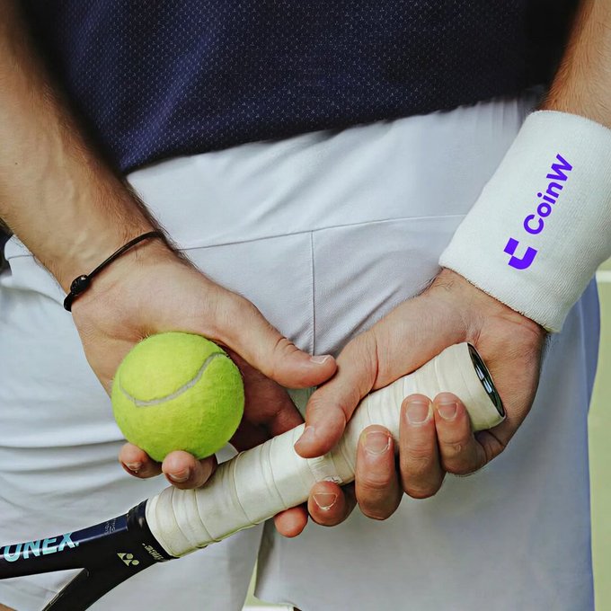 A close-up of a tennis player holding a yellow tennis ball and a Yonex racquet behind their back, wearing white shorts and a white wristband prominently branded with the purple 'CoinW' cryptocurrency exchange logo.