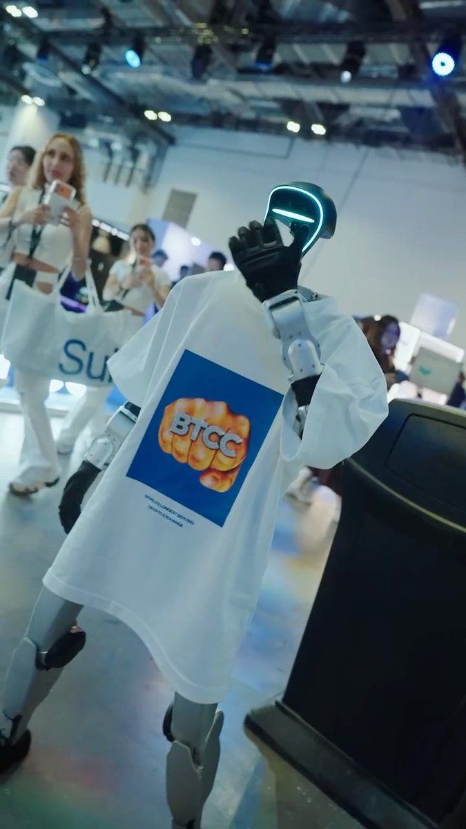 A humanoid robot wearing a white t-shirt featuring a "BTCC" logo poses at the BingX booth during the #TOKEN2049 conference, with attendees visible in the background. The image captures the interactive and tech-forward atmosphere of BingX's presence at the event, which featured games, giveaways, and Web3 discussions.