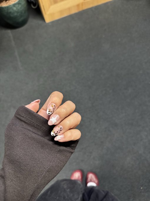 A hand displaying star and leopard print nail art emerges from a fingerless sleeve, with burgundy sneakers visible on the floor below.