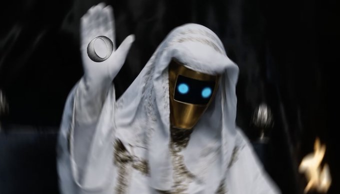 A hooded figure wearing a white robe and a gold robotic mask with glowing blue eyes raises one hand, conjuring or holding a small glowing orb. The mysterious, mystical aesthetic visually matches the cryptic "gordr coming soon." post, suggesting an upcoming reveal with an otherworldly or supernatural theme.