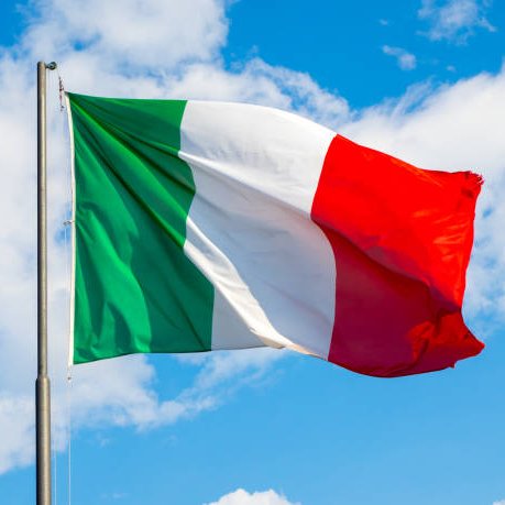 The Italian flag waving on a flagpole against a bright blue sky with scattered white clouds.