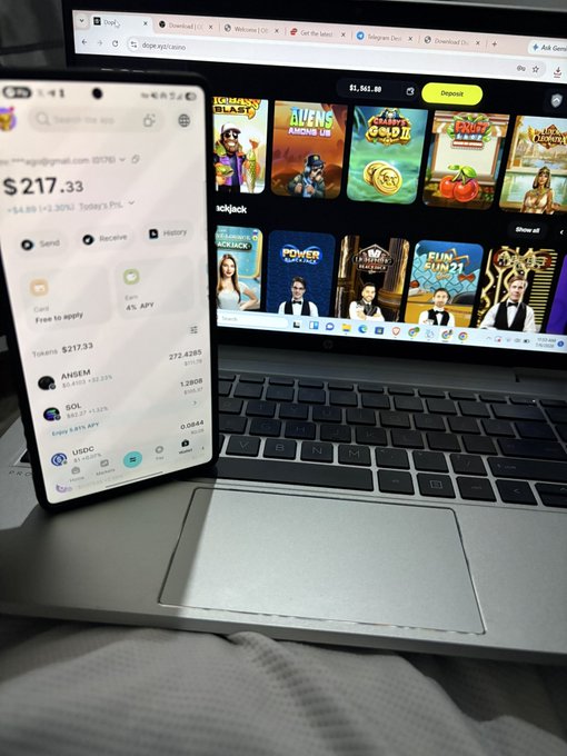 A smartphone displaying a crypto wallet app showing a balance of $217.33 and tokens including ANGEM and SOL sits propped against an open laptop screen featuring various slot games and gambling sites. The image relates to "gN web3" by illustrating the intersection of cryptocurrency holdings with online gambling platforms.