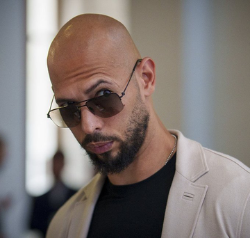 Bald man with sunglasses and a beard wearing a beige blazer over a black shirt, identified as Andrew Tate. The image accompanies news of his large $HYPE token deposit to Binance, reportedly realizing a $7.24M profit.