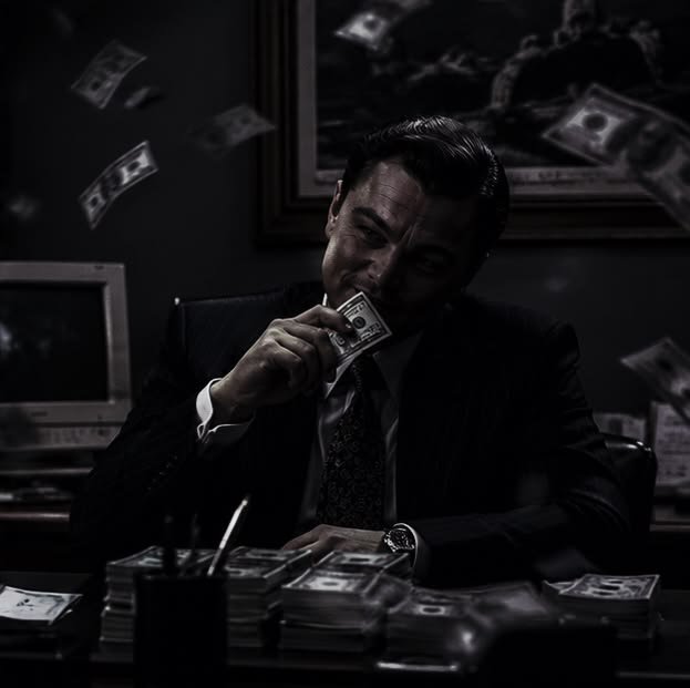 A dark, moody black-and-white image shows a well-dressed man in a suit at a desk, smiling slyly as he brings a stack of cash to his face, with dollar bills raining down around him and piles of money stacked before him — capturing the celebratory, "gains" energy of the crypto pump highlighted in the post.
