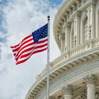 An American flag waves against a cloudy sky in front of the U.S. Capitol's white domed architecture, symbolizing the U.S. government's involvement in the joint statement with the UK regarding stablecoin regulation.