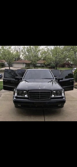 A black Mercedes-Benz sedan is parked in a driveway with all four doors open, with a star emblem visible on the hood.