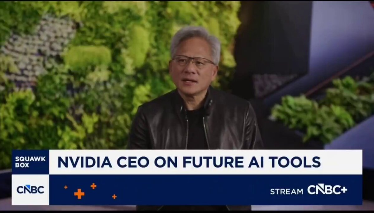 The image shows a man wearing glasses, sitting down with his hands on his lap while talking about artificial intelligence (AI) tools. The text on the screen reads "Nvidia CEO Jensen Huang SAID LIVE ON CNBC THAT AI WILL NEED A SYSTEM OF RECORD" and "focus on what is in the image and how it relates to the post". This suggests that the man might be discussing the importance of AI systems for verifying information, as indicated by the quote from a source.