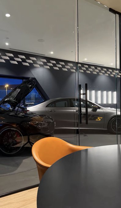 A silver Mercedes-Benz "S" (with the yellow "S" logo visible on its side) and a black sports car with its hood open are displayed behind glass in what appears to be a showroom or luxury lounge. The caption teases that the meeting is "cooking up" something secretive, using the sleek, high-end car imagery as a symbol of the ambitious $SOL-related project being discussed.