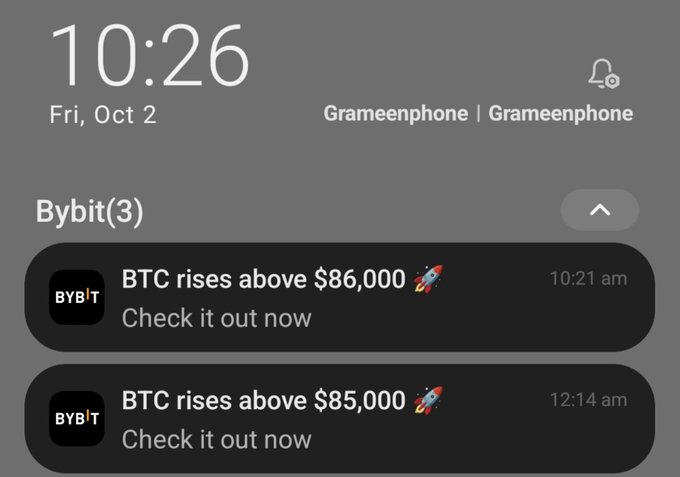 A smartphone lock screen showing the time 10:26 on Fri, Oct 2, displaying notifications from Bybit announcing 'BTC rises above $86,000' at 10:21 am and 'BTC rises above $85,000' at 12:14 am.