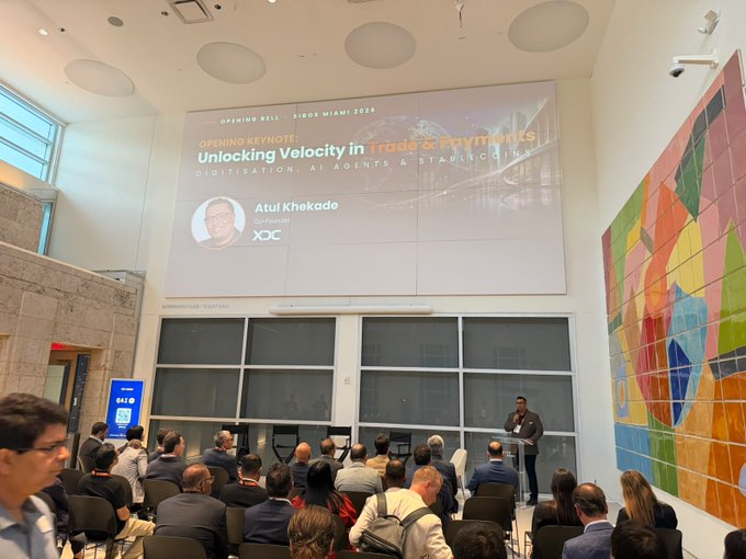 The image captures Atul Khekade, Co-founder of XDC, delivering the opening keynote at the "Unlocking Velocity in Trade & Payments: Digitalisation, AI Agents & Stablecoins" breakfast during Sibos Miami 2026, with attendees seated and listening to the presentation. The scene reflects the event's focus on how digital trade, payments, global standards, and AI are converging to create more connected financial ecosystems.