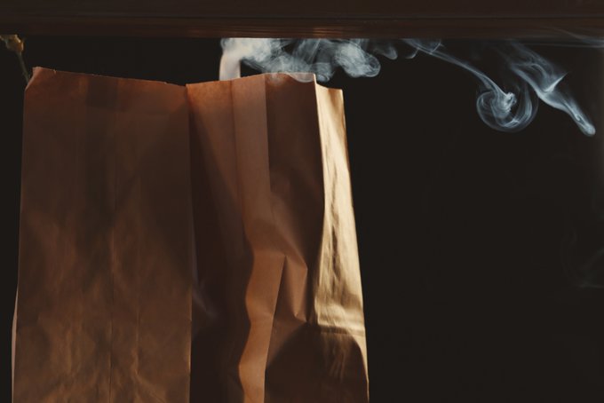 A brown paper bag with wisps of smoke rising from it against a dark background.