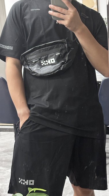 A mirror selfie of a person wearing a black outfit with a black 'DXR' branded fanny pack and matching shorts.