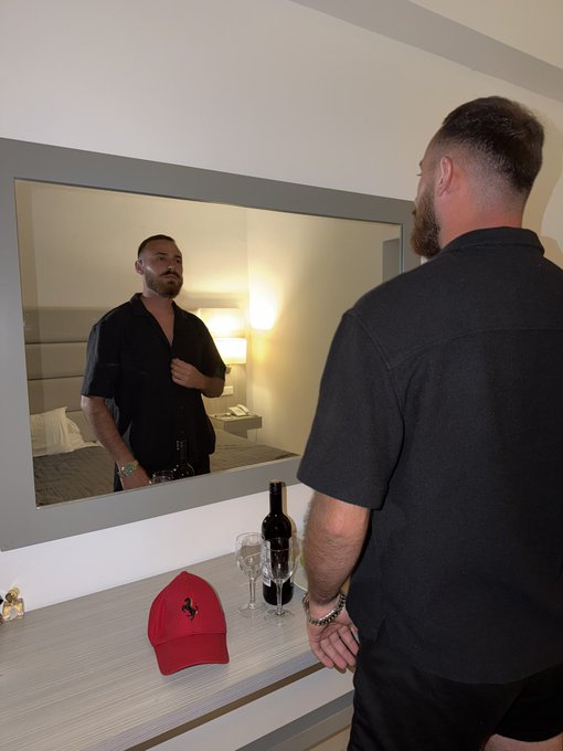 A man in a black shirt looks into a hotel mirror, with a red cap and wine bottle on the counter below—captioning for a chance to win 1 SOL.