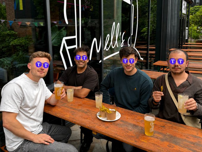 Four men sit at an outdoor wooden table enjoying beers, with the stylized text "Hirell's" visible on the window behind them. The casual post-work drinks scene appears to celebrate the team's efforts as shipping velocity ramps up heading into a busy couple of weeks for $TAO.