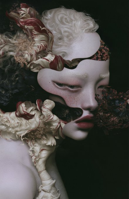 An artistic, surreal portrait of a pale figure with closed eyelids, featuring fragmented facial features intertwined with white curls and large flowers with red-tipped petals against a dark background.
