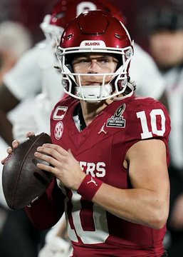 A college football player wearing a crimson Oklahoma Sooners jersey with the number 10 is shown holding a football in throwing position, identified as their quarterback. The image relates to the post about a $79,000 bet on Oklahoma to win by over 4.5 points against Michigan on Polymarket.