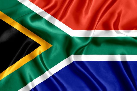 A close-up rendering of the South African flag showing its red, blue, green, black, white, and yellow colors in a Y-shape design.