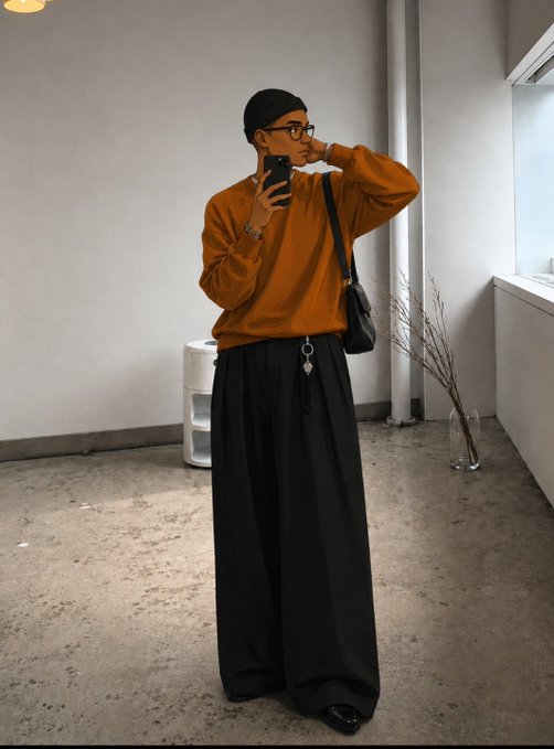 A stylish person taking a mirror selfie, wearing a black beanie, glasses, an oversized orange/rust sweatshirt, and wide-leg black pants, with a black crossbody bag, standing in a minimalist concrete space.