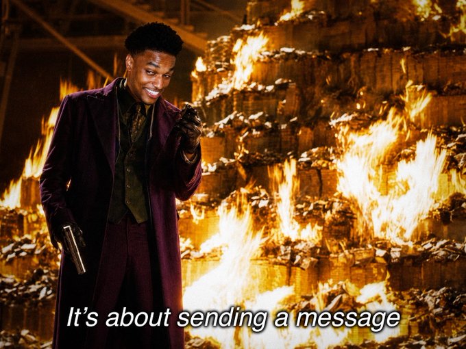 A man in a maroon coat stands before a massive wall of money on fire, declaring "It's about sending a message"—a fitting visual metaphor for confidently holding through the $ANSEM dip rather than panic selling.