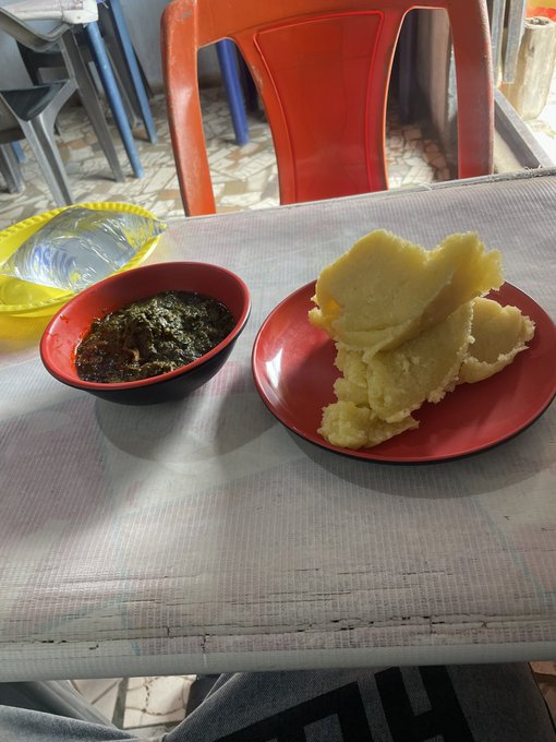 A meal of fufu (yellow dough) and a dark green soup served on red plates sits on a table.
