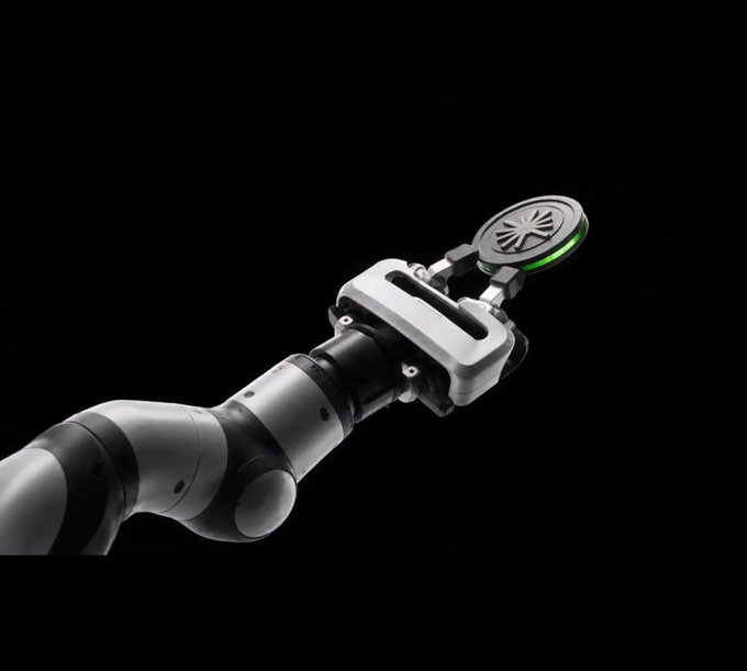 A sleek robotic arm with a silver and black design gripping a circular object with a starburst pattern, set against a black background.